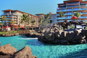 Un resort con piscina cristalina, palmeras y edificios de varios pisos con balcones.