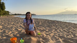 A sandy beach with a person kneeling, a bucket, and a green shovel.