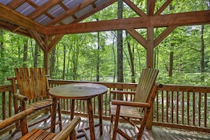 Enjoy a serene forest view from this elevated deck with a round table and two chairs.