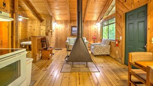 L’intérieur d’une cabane en rondins, avec un poêle à bois au centre, des murs en bois et une porte verte.