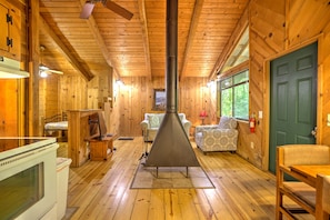Cozy cabin interior with a central wood-burning stove, dining area, and seating space.