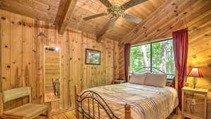 Une chambre à coucher dans une cabane en bois, comprenant un lit, une chaise, une table de chevet, une lampe et un ventilateur de plafond.