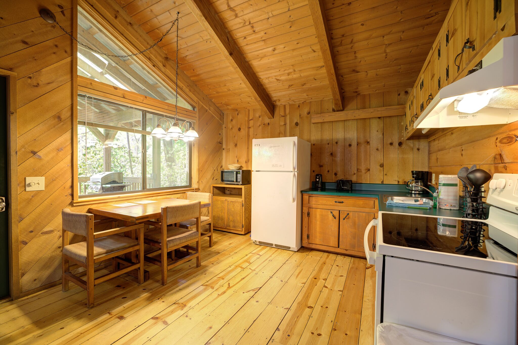 A wooden cabin kitchen with a dining table, chairs, a refrigerator, a microwave, and a stove.