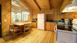 Une cuisine rustique aménagée dans une cabane en bois, avec une table à manger, des chaises, un réfrigérateur, un four à micro-ondes et une cuisinière.