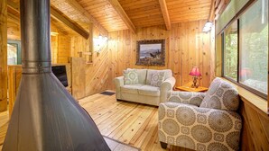 L’intérieur d’un chalet chaleureux, avec une cheminée, des murs en bois, un canapé et une fenêtre.