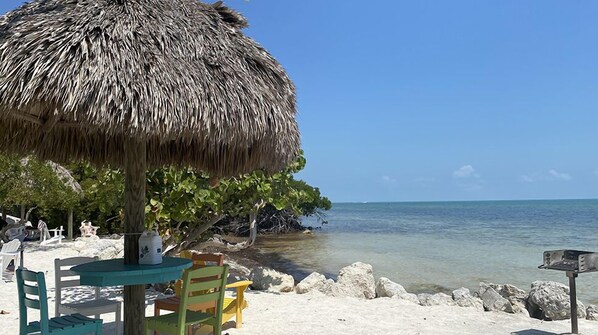 Relax under a shaded table with a view of the calm ocean and surrounding rocks.