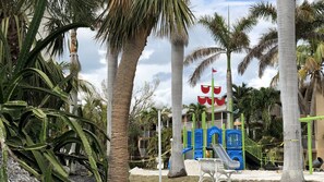 Kids can play on the playground surrounded by palm trees.