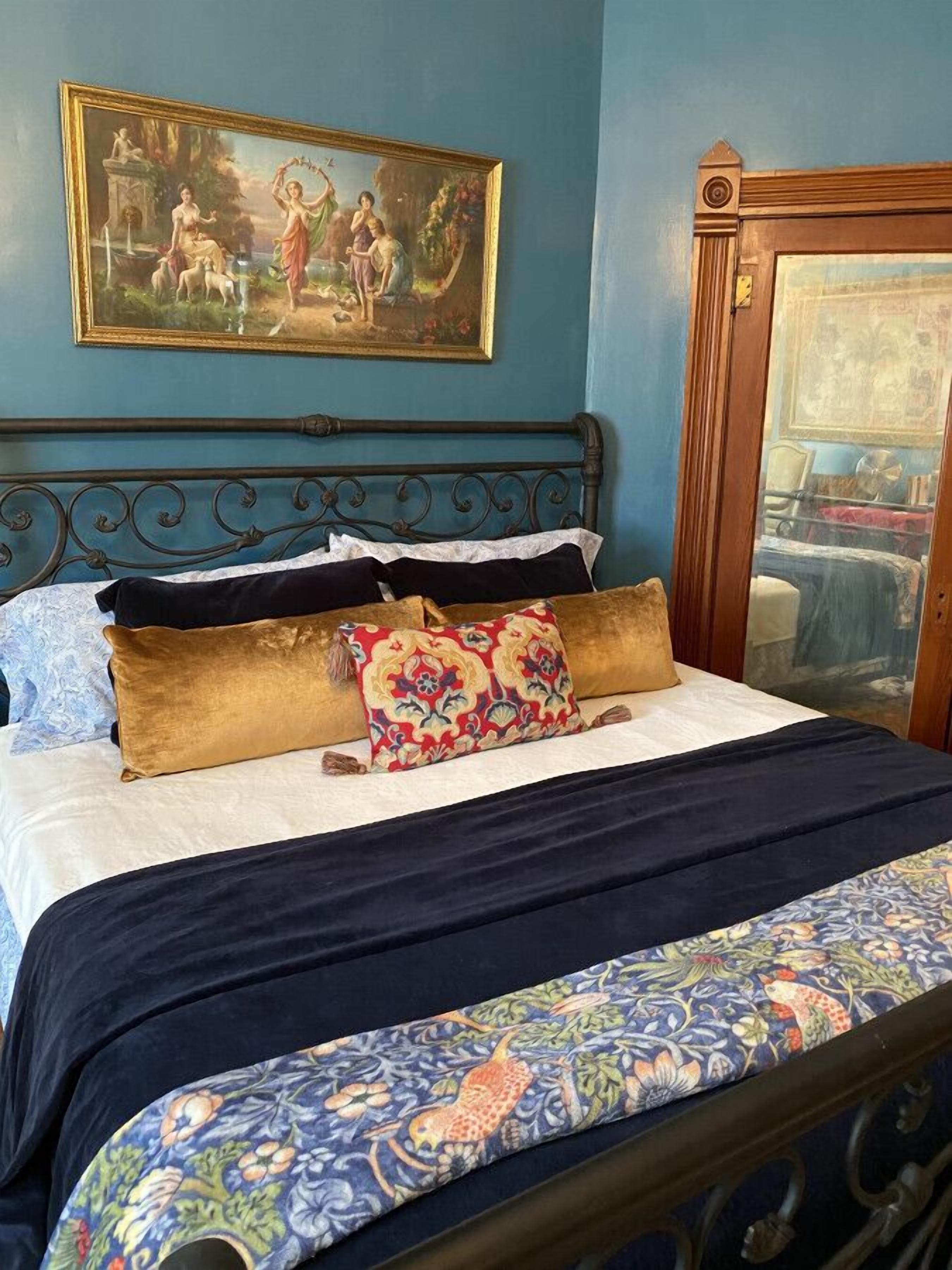 A bed with a patterned bedspread, a blue wall, and a framed painting above the bed.