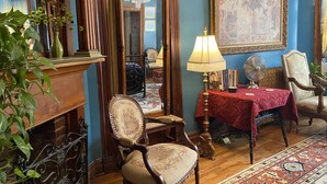 Una habitación con una silla de madera, una mesa con mantel rojo, un espejo y una araña.