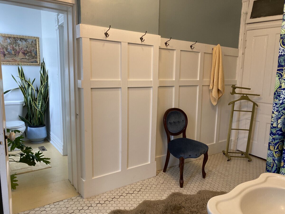 A bathroom with a white vanity, a chair, a towel rack, and a potted plant.