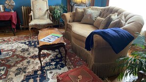 Una sala de estar con un sofá, un sillón, una mesa de centro, un tapete estampado y un cuadro grande en la pared.