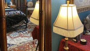 Una habitación con un espejo grande, dos lámparas de mesa, una cama con colcha estampada, una mesa roja y suelo alfombrado.