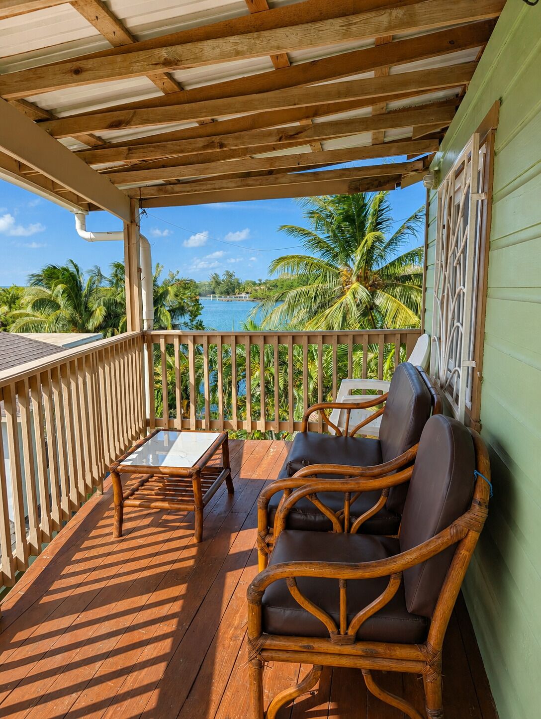 A wooden deck with a table and chairs, overlooking a body of water and palm trees.
