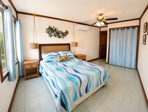 Een slaapkamer met een bed, nachtkastjes, een plafondventilator en uitzicht op het omliggende landschap.