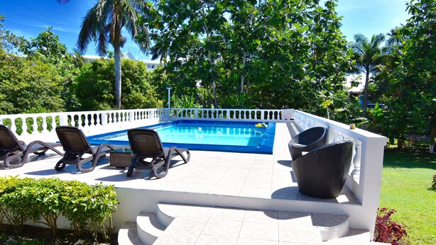 A poolside area with a white tiled deck, lounge chairs, and a white fence. - The Cottage very comfortable, relaxing also secure, 5 minutes walk from beach (Ocho Rios)