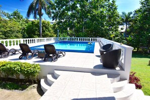 A poolside area with a white tiled deck, lounge chairs, and a white fence. - The Cottage very comfortable, relaxing also secure, 5 minutes walk from beach (Ocho Rios)