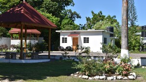 A gazebo with a red roof, a white building with a wooden door, and a garden with rocks and plants. - The Cottage very comfortable, relaxing also secure, 5 minutes walk from beach (Ocho Rios)