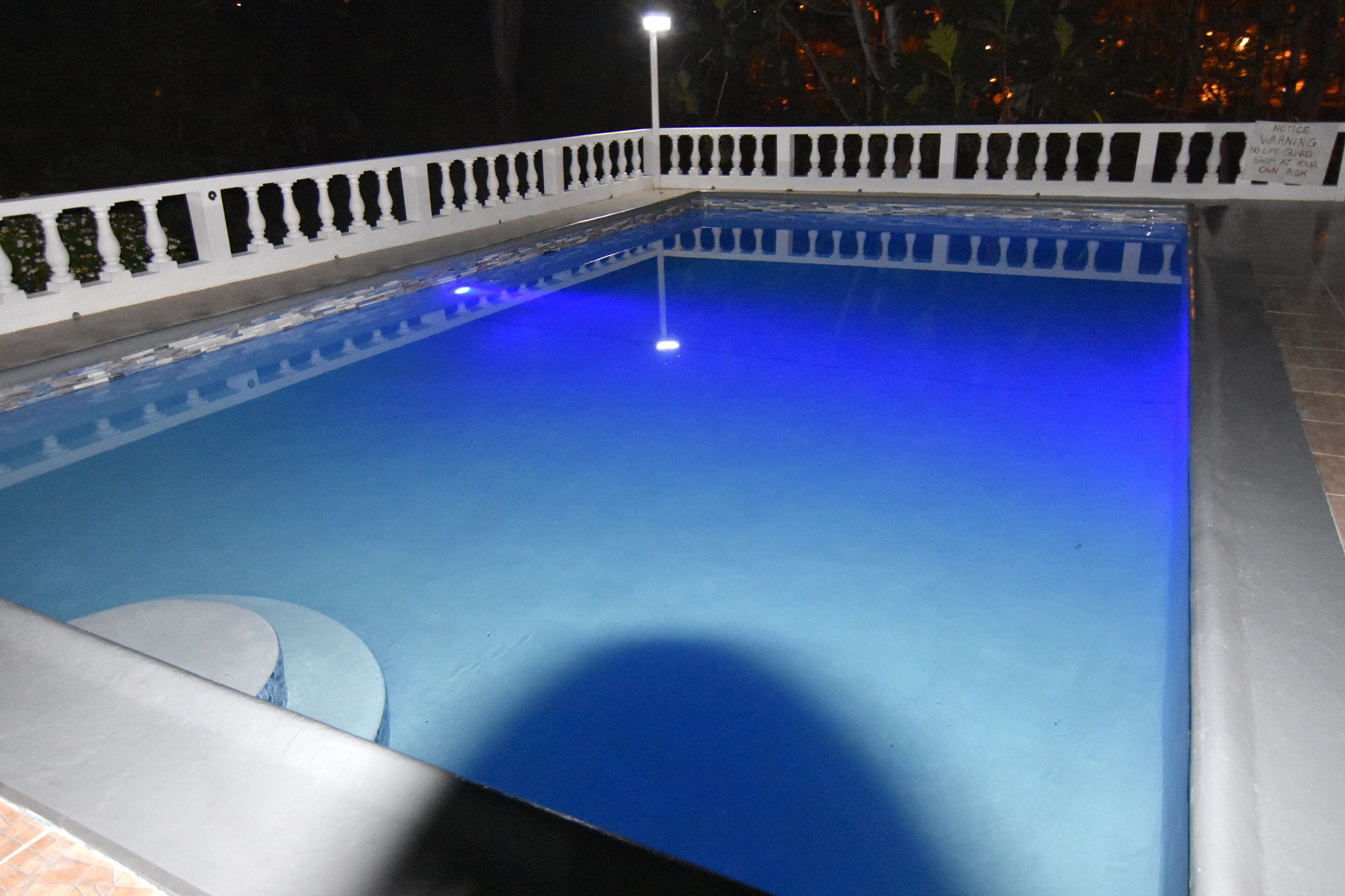 Une piscine bordée de blanc et un seul lampadaire.