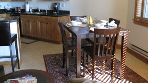 A dining area with a wooden table, chairs, and a kitchen in the background. - Flathead Waterfront 2BR/2BA Condo @ Waterside (Lakeside)