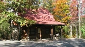 A rustic cabin with a red roof, surrounded by trees with autumn foliage.