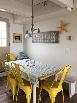 A dining area with a table, yellow chairs, a starfish decoration, and a 'Let's Do Sunset' sign. - Oceanfront With Memorable Surf And Haystack Rock Views (Pacific City)