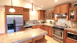 A modern kitchen with wooden cabinets, a granite countertop, stainless steel appliances, and pendant lighting.