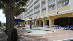 A hotel pool area with lounge chairs, umbrellas, and a palm tree.