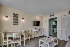 A dining area with a table and chairs, a small console table with a TV, and a kitchen visible through an open door.