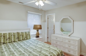 Cozy retreat with a large bed, nightstand, and dresser, plus a ceiling fan and window with blinds.