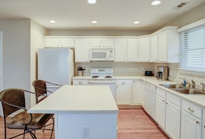 Kitchen features a central island, refrigerator, microwave, stove, dishwasher, sink, and window with blinds.