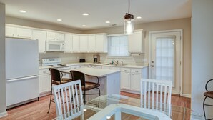Una cocina moderna con armarios blancos, una mesa de comedor de vidrio y una lámpara colgante.
