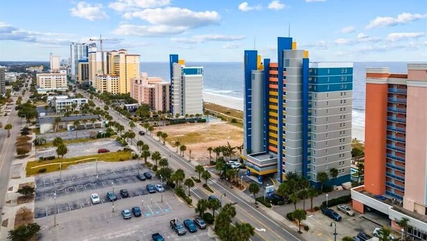 A coastal cityscape with high-rise buildings, a parking lot, and a beach in the background.
