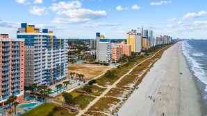 A coastal hotel with multiple high-rise buildings, a beach, and a clear sky.