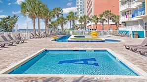 A swimming pool area with lounge chairs, palm trees, and a building in the background.