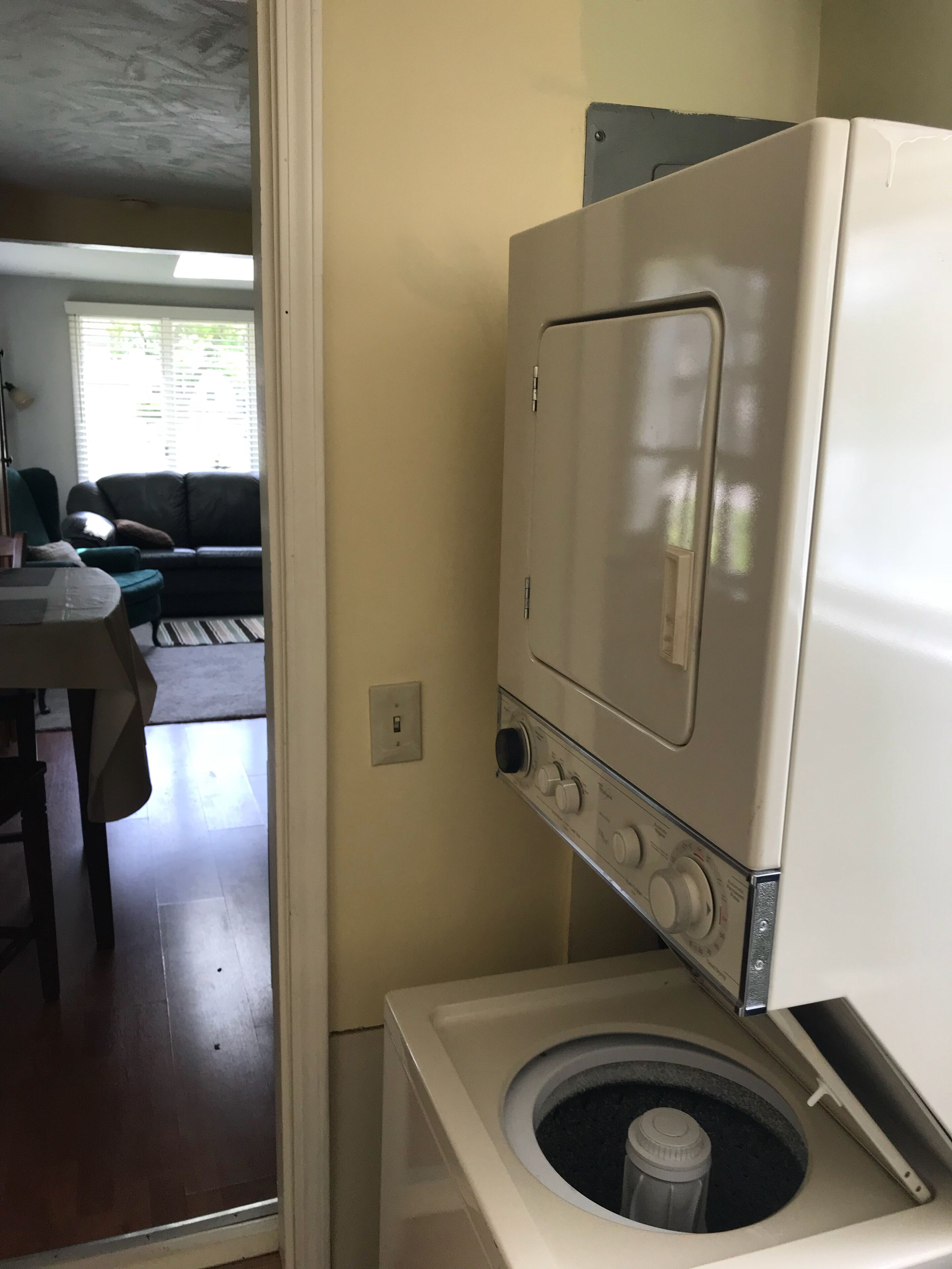 A compact laundry room with a front-loading washing machine and dryer, a small table with a chair, and a couch in the background.