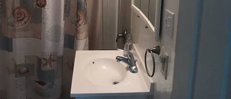 A bathroom with a shower curtain featuring sea shell and starfish patterns, a white sink with a modern faucet, and a mirror with a decorative frame.