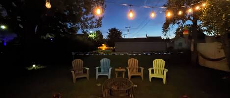 An outdoor seating area with string lights, four Adirondack chairs, and a metal table with a lantern.