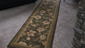 Una sala de estar con un sofá de cuero negro, un sillón verde, un tapete floral y una pared de acento de piedra.