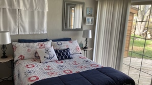 Un dormitorio con una cama, dos mesitas de noche, una ventana con cortinas y vistas al exterior.