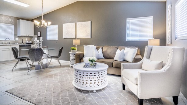 Een moderne woonkamer met een grijze bank, witte fauteuils, een ronde salontafel en een eethoek met een glazen tafel en stoelen.