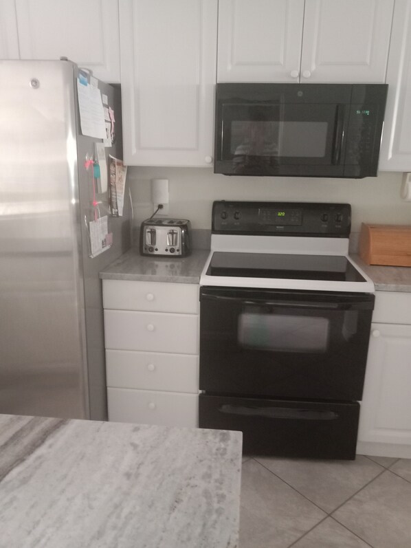 Una cocina con armarios blancos, un refrigerador de acero inoxidable, un microondas negro, una estufa y un tostador.
