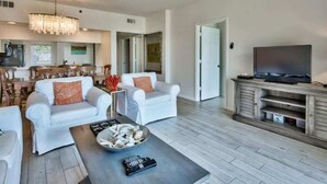 A spacious living room with a dining area, a television, and a chandelier. - Pool Front at High Pointe Resort-Ground Floor Unit (Panama City Beach)