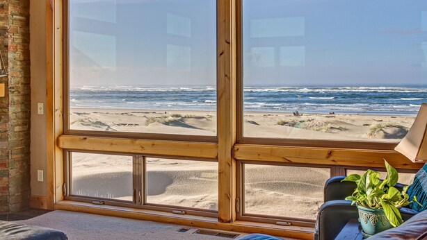 Ein Zimmer mit großen Fenstern mit Blick auf einen Strand, einer Topfpflanze und einer hölzernen Bank.
