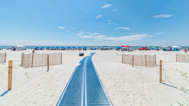 Een strandpad dat naar de zee leidt, met parasols en mensen op de achtergrond.
