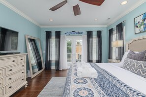 A bedroom with a bed, a dresser, a ceiling fan, and a window with curtains.