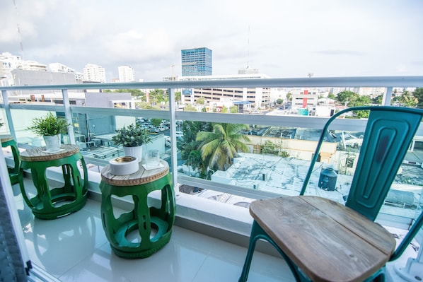 Enjoy the city view from this balcony with a chair and stools, surrounded by lush plants.