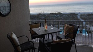 Ein Balkon mit Tisch und Stühlen mit Blick auf einen Strand bei Sonnenuntergang.