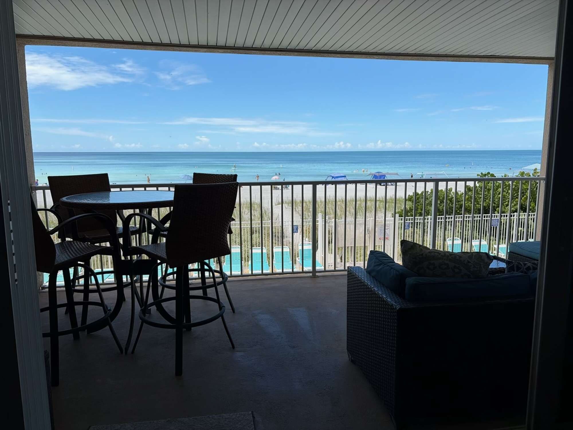 A balcony with a view of the beach and ocean, furnished with a table, chairs, and a sofa.