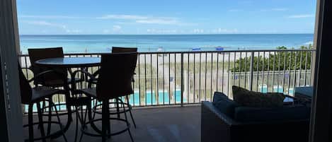 A balcony with a view of the beach and ocean, furnished with a table, chairs, and a sofa.