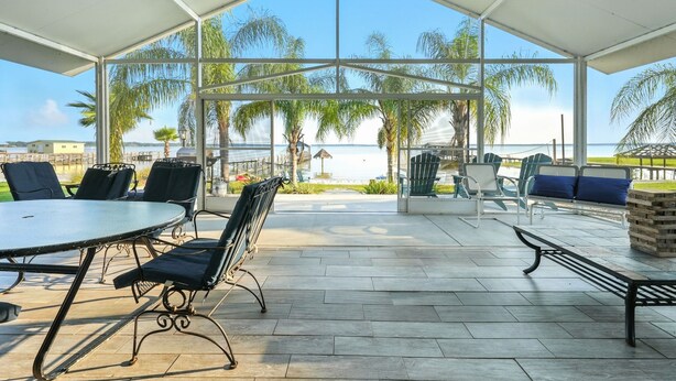 Un espacio al aire libre cubierto con una mesa y sillas, un banco y vistas a la playa y palmeras.